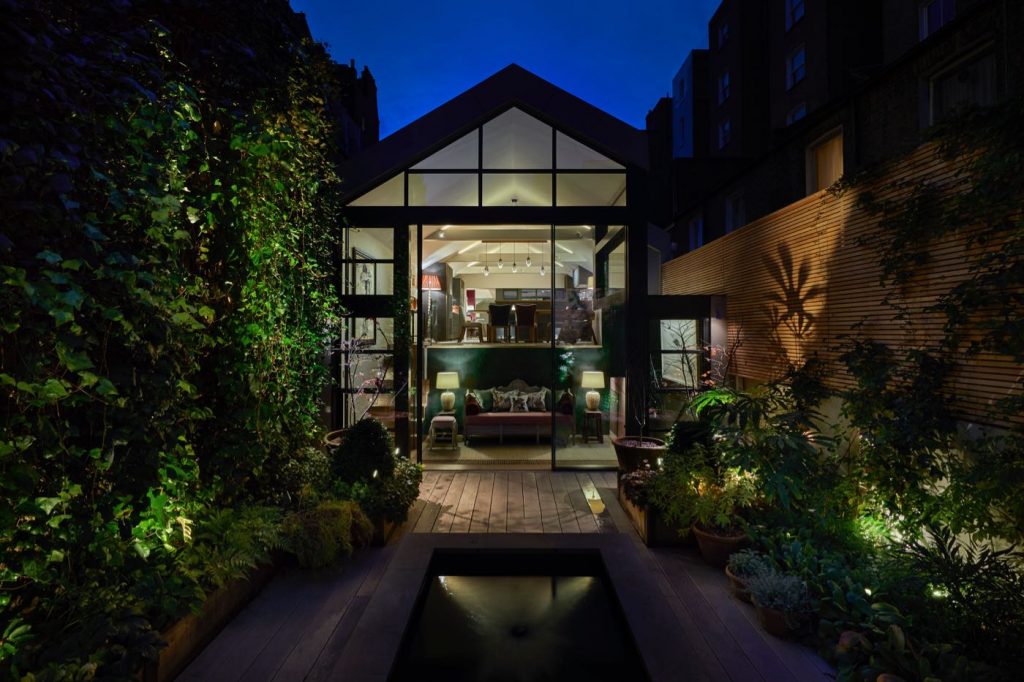 Garden of modern London house with pond and wooden slatted wallsdesigned by Tania Compton and lit by John Cullen