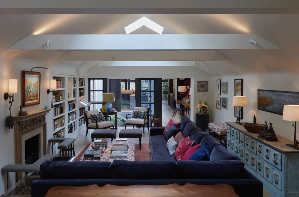 London house sitting room with large L shaped velvet sofa, pasta cabinet and carved antique wood fire surround